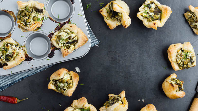 Puff pastry cups both in and outside of a muffin tin filled with  vegetables and cheese