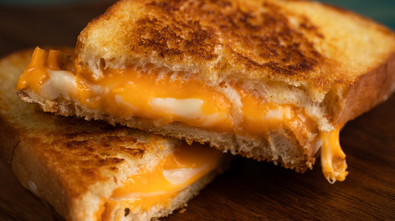 A gooey grilled cheese sandwich cut into two pieces on a wooden surface.