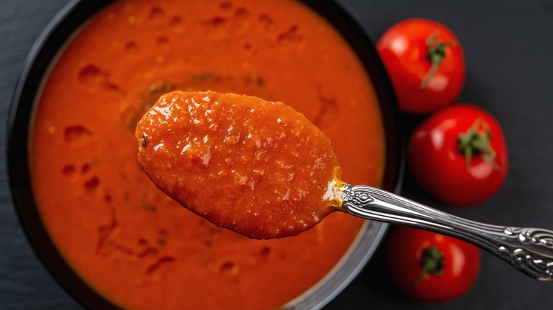 A close-up of thick tomato soup in a spoon over a bowl.