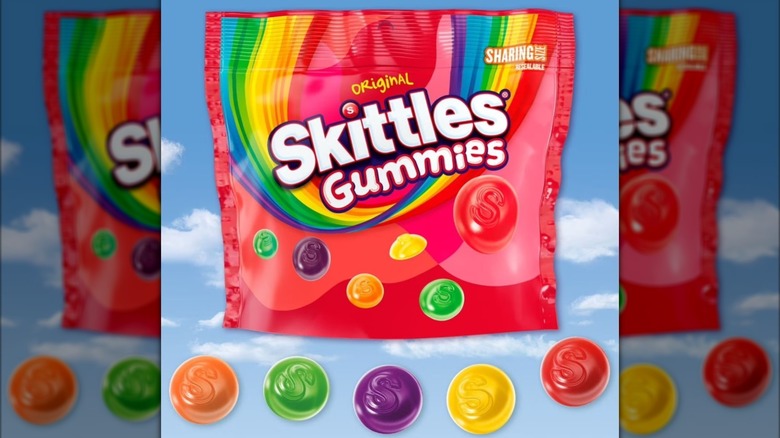 A bag of Skittles Gummies candies against a blue sky backdrop with clouds.