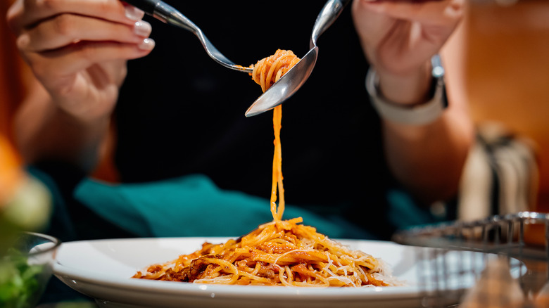 A woman twirls spaghetti onto a fork using a spoon