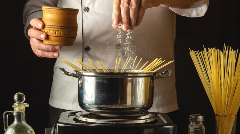 A cook salting pasta water as he prepares to boil pasta.
