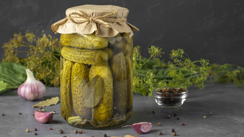 cucumbers pickling in a jar with verbs, water, and vinegar in it.