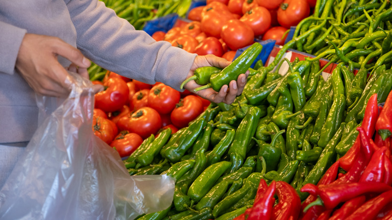 A customer at a grocery store holds up a green spicy pepper that's been picked off a shelf of multiple spicy peppers