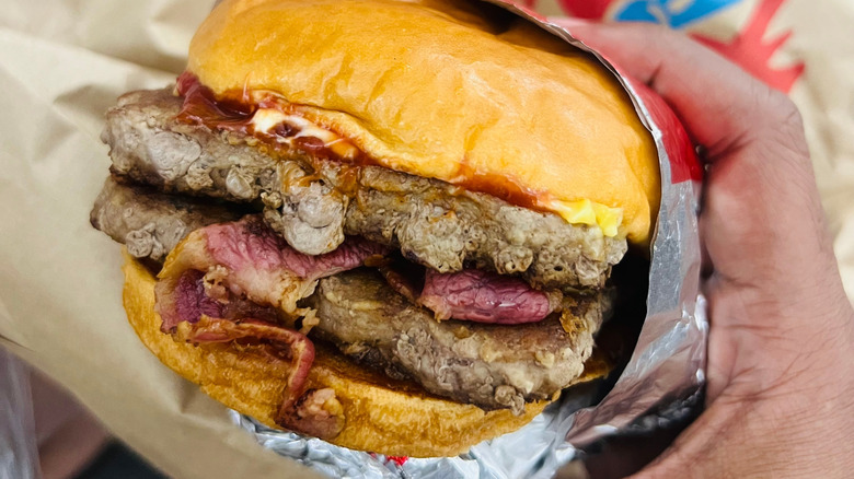 A closeup of a hand holding a Wendy's burger with two patties, bacon, and cheese