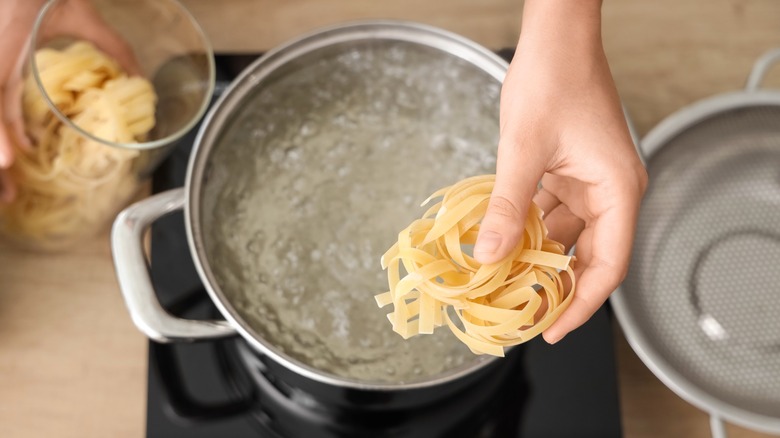 Hand putting ring of pasta into boiling water
