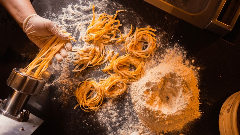 Person making fresh pasta and arranging it in rings near a pile of flour