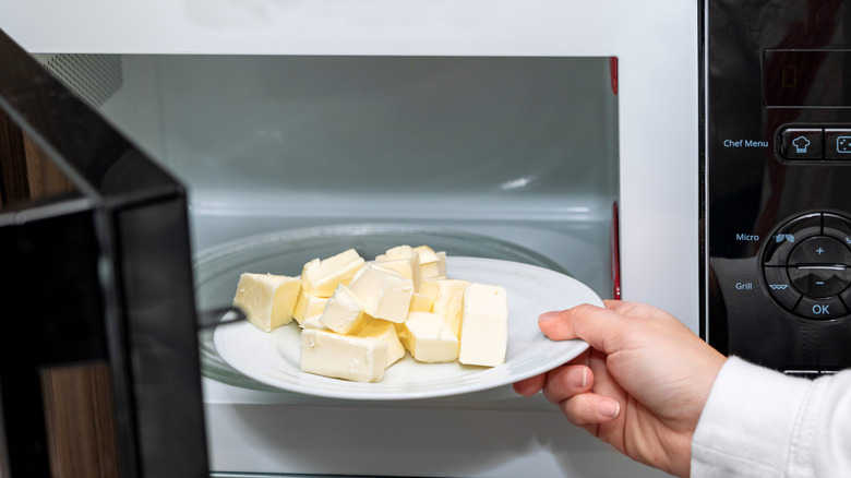 Hand placing a plate of butter in a microwave