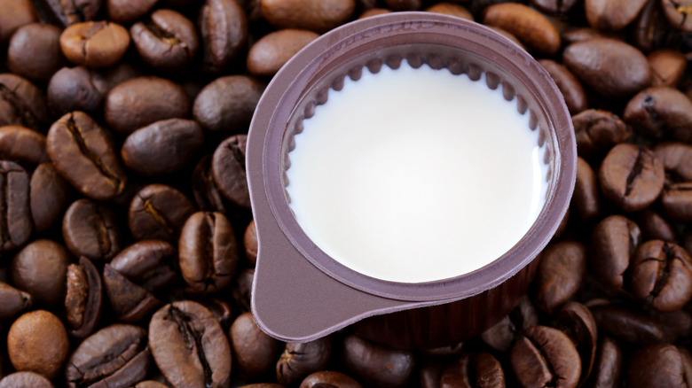 A small cup of coffee creamer on top of a pile of coffee beans