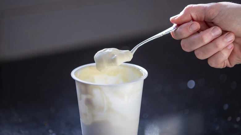 A spoon coming out of a tub of yogurt