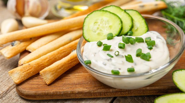 A bowl of tzatziki sauce next to a pile of breadsticks