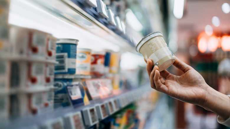 A customer's hand holding a yogurt container at a dairy aisle