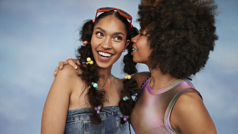 A woman whispers a secret into her friend's ear