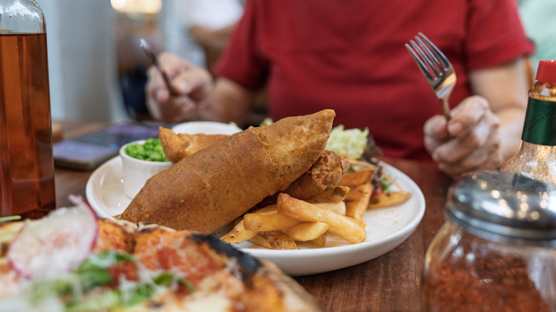 A diner enjoying fish and chips and other accompaniments on the table