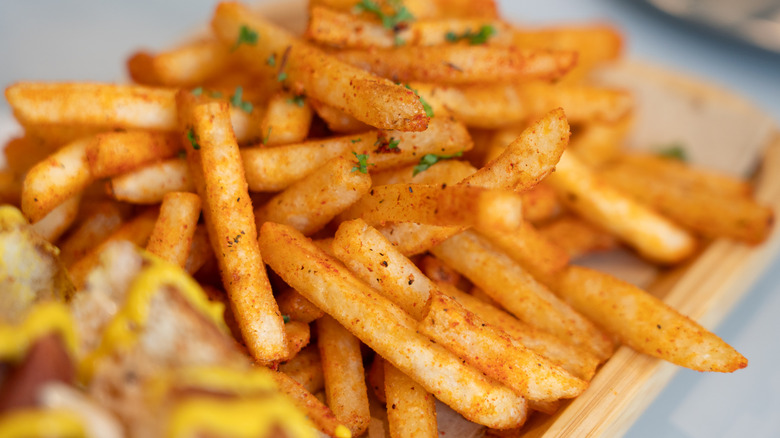A pile of French fries on a wooden serving tray, partially in focus