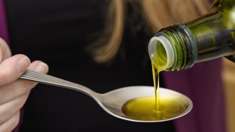 A woman pouring a spoonful of olive oil, presumably to taste it.