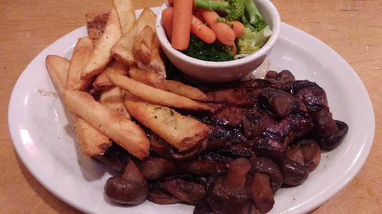 A plate of food at Texas Roadhouse with steak, mushrooms, fries, and vegetables.