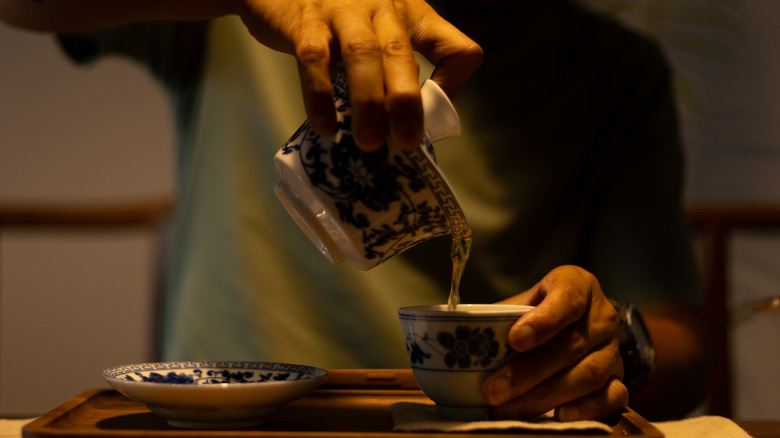 A person pouring tea to drink using traditional chinaware