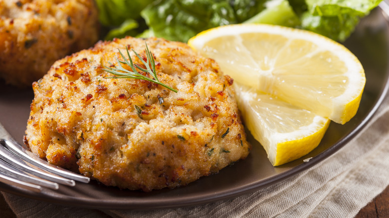 Golden brown crab cake on a brown plate with two lemon slices