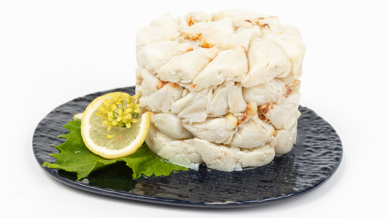 Large white crabmeat lumps in the shape of a tall can on a round black plate with a lemon slice