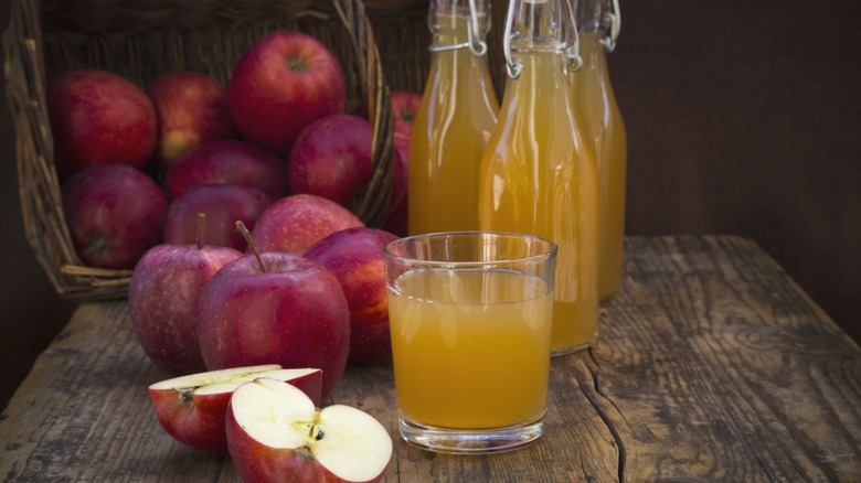 Glasses and bottles of fresh apple juice, next to a basket of apples