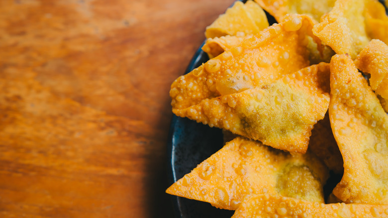 Crispy deep fried golden wonton wrappers served on black plate over wooden table.