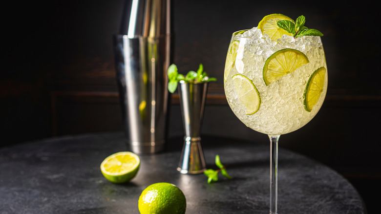 A margarita in a wine glass filled with ice and lime slices on a black table.