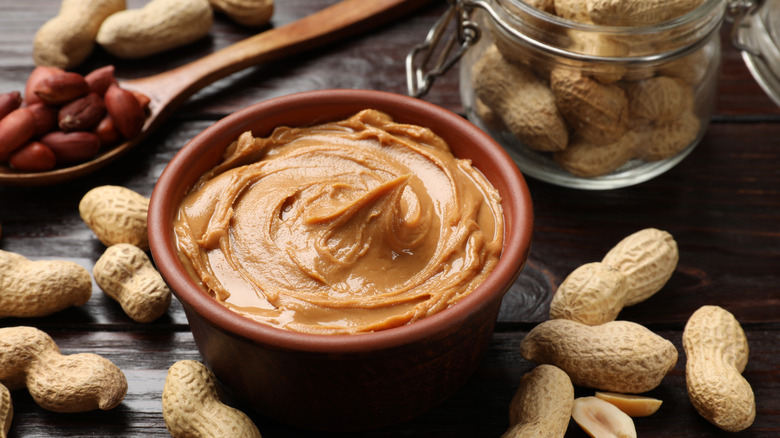 A small container of peanut butter surrounded by peanuts on a table