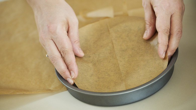Hands placing paper circle in  round cake pan
