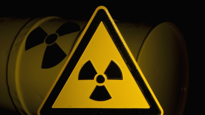 A sign displaying the radiation symbol, in front of a barrel that has the same symbol on it.