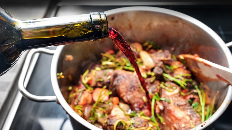 Red wine poured from bottle into stock pot with meat and vegetables