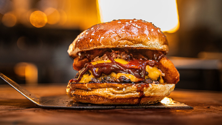 A double smash burger with cheese and sauce in a sesame seed bun on a spatula