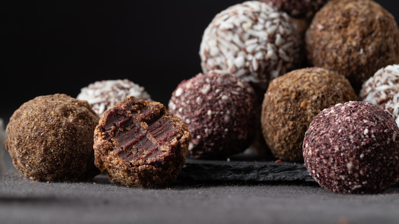 A pile of chocolate truffles with various toppings, one truffle has a bite in it