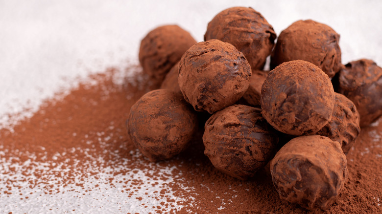 Cocoa-dusted chocolate truffles are piled on a white counter with more cocoa powder around them