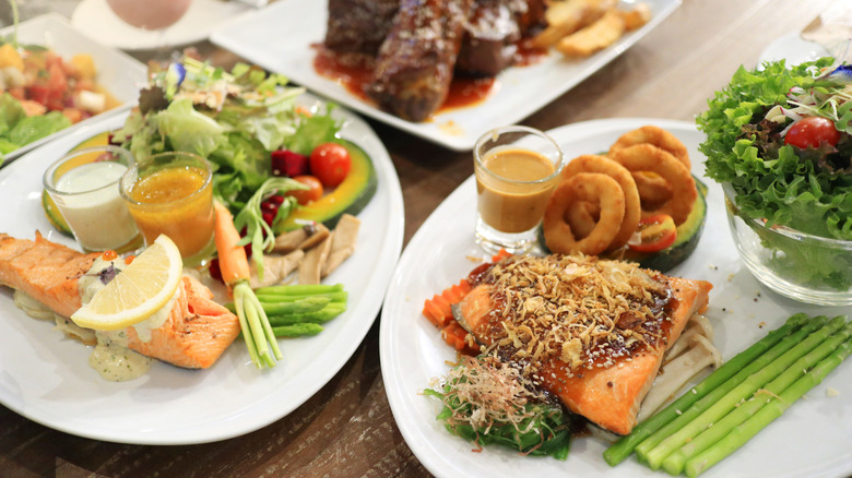 A teriyaki salmon dinner sits on a table next to two salads