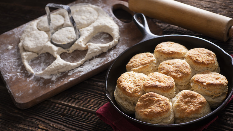 Buttermilk biscuits cooked in a cast iron skillet on a wooden table with ingredients on a cutting board