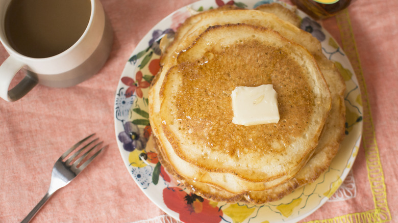 A short stack of golden brown pancakes with a pat of butter and coffee