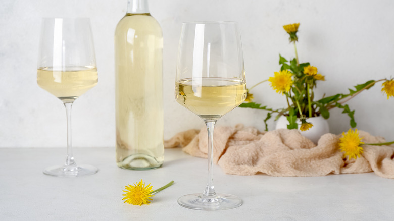 Pale yellow dandelion wine in a bottle and two glasses with fresh dandelion weed