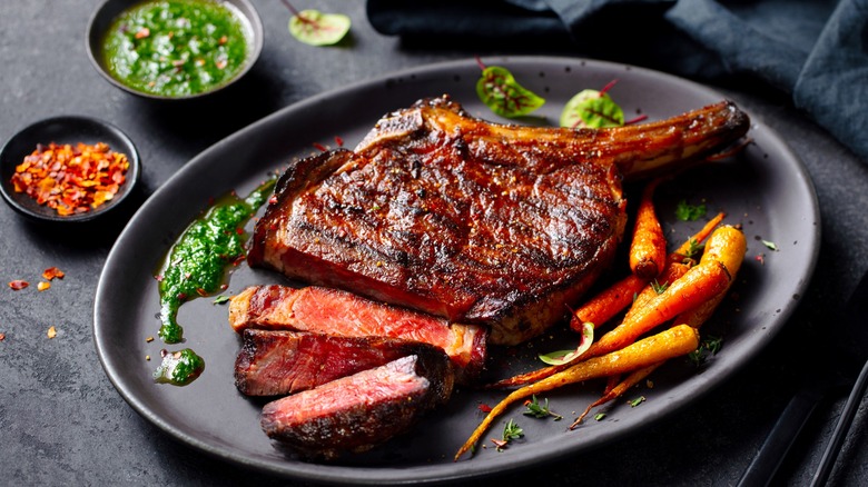 Tomahawk steak with chimichurri sauce and carrots on a black plate