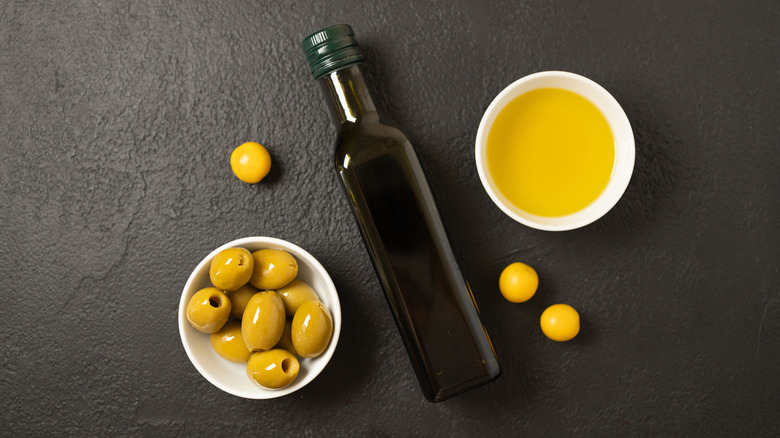 A bottle of olive oil next to olives on a black surface.