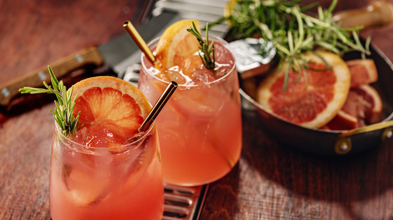 Two glasses of Paloma cocktails with slices of grapefruit and sprigs of rosemary