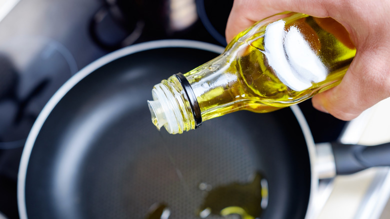 Olive oil being added to a black pan on a stove