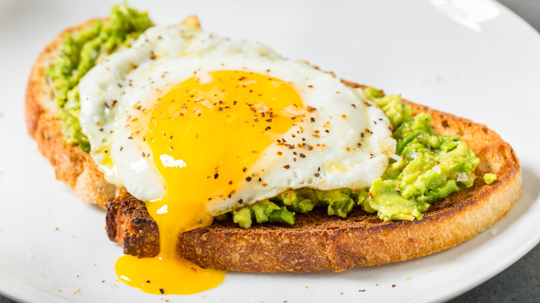 Over easy egg with yolk dripping down on piece of avocado toast