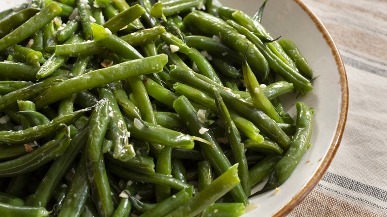Cooked and seasoned green beans in white bowl close up