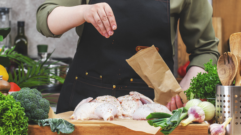 A hand seasoning raw chicken from above