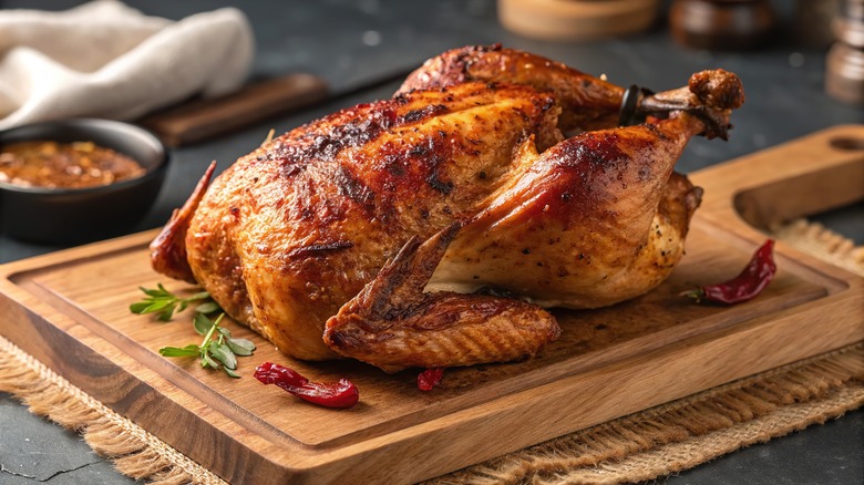 A roast chicken with golden skin on a wooden cutting board