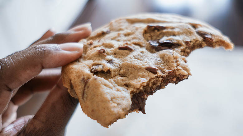 A hand holding a half-eaten chocolate chip cookie