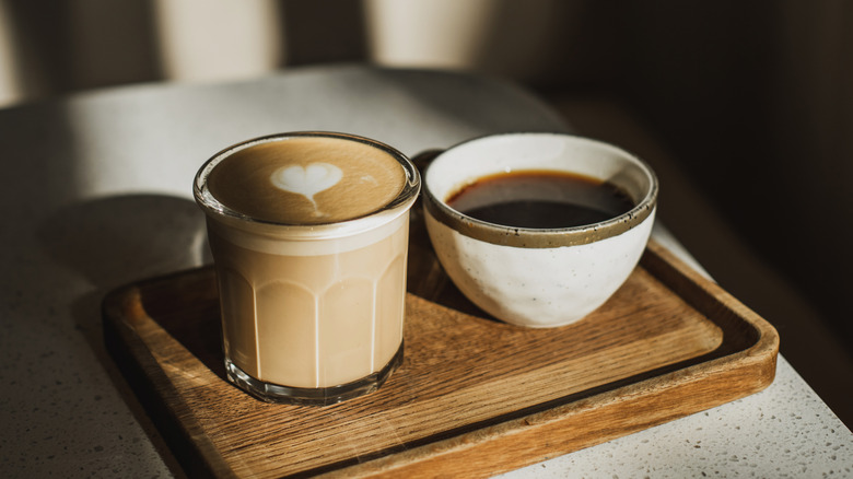 A white ceramic cup of coffee and a glass cup of coffee on a wooden tray