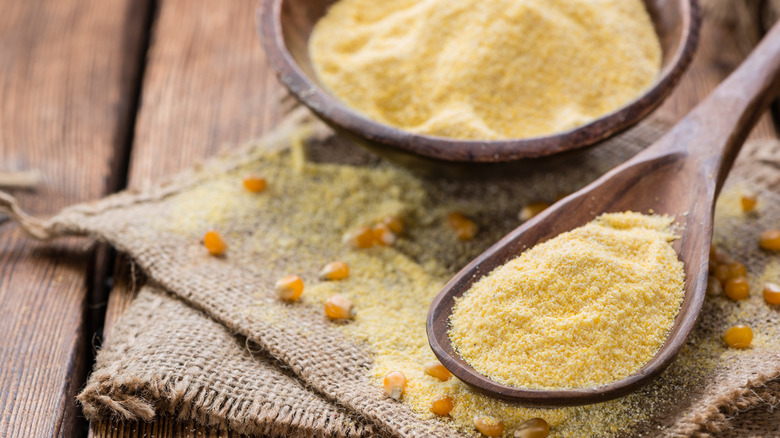 Cornmeal in wooden bowl and spoon alongside scattered corn kernels