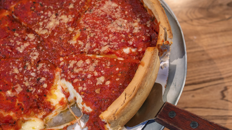 Giordano's stuffed crust pizza in a metal pan on a wooden table with a pizza server